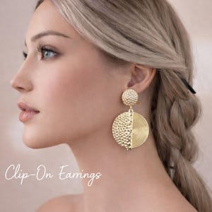 Könnte beinhalten: Goldene Clip-On-Ohrringe. Die Ohrringe haben eine strukturierte, kreisförmige Oberseite und eine größere, halb strukturierte, halb gerillte kreisförmige Unterseite. Der Text "Clip-On Earrings" ist in Kursivschrift auf dem Bild geschrieben.