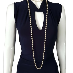Op de afbeelding: Twee parelkettingen op een mannequin. De ene is een lange, enkele streng en de andere is een kortere choker met dubbele streng. Beide kettingen hebben kleine, ronde, witte parels geregen aan een goudkleurige ketting. De mannequin draagt een mouwloze, marineblauwe jurk.