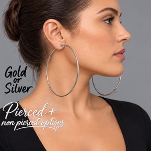 May include: Large, thin, circular silver hoop earrings. The text on the image reads Gold or Silver and Pierced + non pierced options. These earrings are designed as a simple, continuous metal loop that rests against the side of the face.