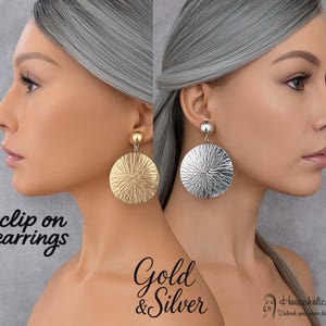 May include: Gold and silver clip-on earrings. The earrings have a large, textured, circular design. The gold earring has a gold ball stud, and the silver earring has a silver ball stud. The text "Gold & Silver" is below the earrings.