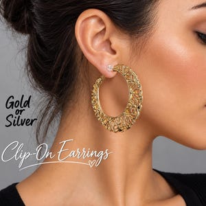 Può includere: Un orecchino a cerchio color oro con un intricato motivo a filigrana traforato. L'orecchino è un modello a clip e presenta un design circolare. Il testo sull'immagine recita: Gold or Silver Clip-On Earrings.