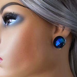 May include: A pair of blue clip-on earrings with a faceted design. The earrings are made of glass and have a dark blue colour with iridescent highlights.