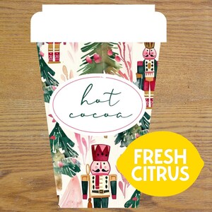 May include: A paper coffee cup with a festive design featuring nutcrackers, Christmas trees, and the words "hot cocoa." A yellow lemon-shaped sticker with the words "fresh citrus" is on the right side of the cup.
