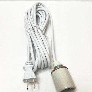 Puede incluir: Un cable eléctrico blanco con un enchufe estándar de dos clavijas en un extremo y una toma de luz de cerámica en el otro extremo.