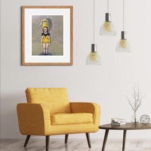 May include: A framed painting of a person wearing a yellow dress with a bird on their head. The painting is set against a light brown wall with a yellow armchair and a wooden coffee table in the foreground.