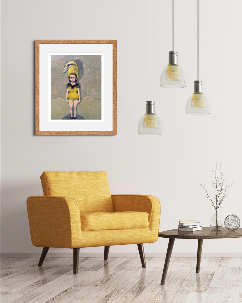 May include: A framed painting of a person wearing a yellow dress with a bird on their head. The painting is set against a light brown wall with a yellow armchair and a wooden coffee table in the foreground.