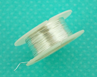 May include: A spool of silver wire on a white plastic spool. The wire is wound tightly and is ready to be used for crafting or jewelry making.