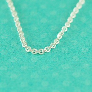 May include: A silver chain necklace with a delicate, linked design. The chain is on a turquoise background.
