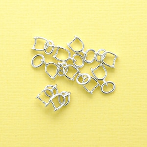 Puede incluir: Un grupo de anillos de salto de metal plateados, también conocidos como anillos de bucle, sobre un fondo amarillo. Estos anillos se utilizan para la fabricación de joyas y la artesanía.