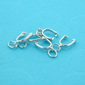 May include: Four silver-toned metal clasps for jewellery making. The clasps are in the shape of a loop with a small ring on one end. The clasps are on a blue background.