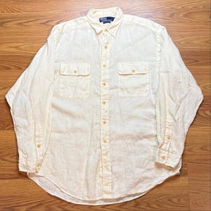 Op de afbeelding: Een overhemd met lange mouwen en knoopsluiting in een bleke crèmekleur. Het overhemd heeft een puntige kraag, twee borstzakken met knoopsluitingen en een centrale knoopsluiting. Een Polo by Ralph Lauren label is zichtbaar in de kraag.