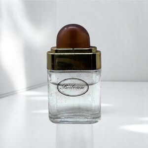 May include: A clear glass bottle with a brown cap and gold-colored accents. The bottle has a rectangular shape with a rounded top and a label that reads "Borbonese". The bottle is likely for perfume or cologne.