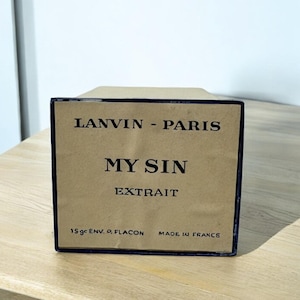 May include: A rectangular box with the text "LANVIN - PARIS MY SIN EXTRAIT" in black. The box is a light brown color with a dark blue border. The text "15 gr ENV. O. FLACON MADE IN FRANCE" is also visible.