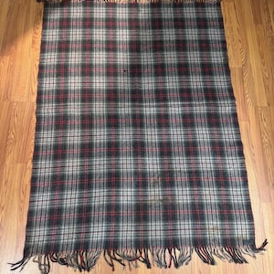 May include: A black, red, and white plaid throw blanket with fringe on all sides. The blanket is made of wool and has a worn look.