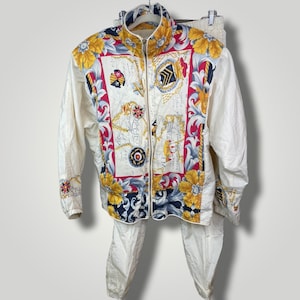 May include: White tracksuit with a colorful map print on the jacket. The jacket has a zipper closure and a stand-up collar. The pants are plain white.