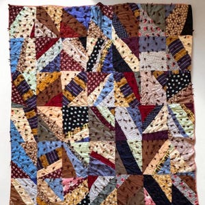 May include: A patchwork quilt with a geometric design. The quilt features a variety of fabrics in shades of blue, brown, red, and cream. The quilt is made of squares and triangles, creating a unique and colorful pattern.