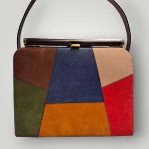 Könnte beinhalten: Eine Vintage-Patchwork-Handtasche mit einem dunkelbraunen Griff. Die Tasche hat eine rechteckige Form mit einem Metallverschluss und besteht aus verschiedenen Lederflicken in Braun-, Blau-, Orange-, Grün-, Beige- und Rottönen. Das Design der Tasche ist eine Mischung aus Farben und Texturen.
