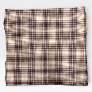 May include: Folded square of fabric with a brown, tan, and blue plaid pattern. The fabric has a classic, woven texture, and the plaid design is evenly spaced across the surface. The overall color palette is neutral, with a mix of warm and cool tones.