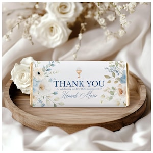 Puede incluir: Una tableta de chocolate con envoltorio blanco con diseños florales en azul, melocotón y verde. El texto "THANK YOU" está sobre el nombre "Hannah Marie", celebrando la Primera Comunión.