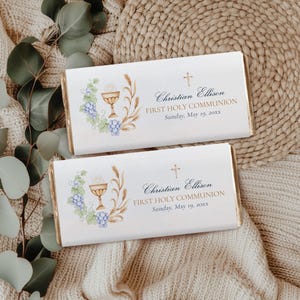 Puede incluir: Dos envoltorios de barra de chocolate blanco con ribetes dorados. Los envoltorios presentan un cáliz dorado, uvas y trigo. El texto en los envoltorios dice "Christian Ellison Primera Comunión Domingo, 19 de mayo de 20XX".