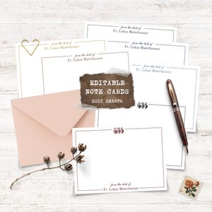 Könnte beinhalten: Eine Sammlung weißer Notizkarten mit braunem Rand, einem rosafarbenen Umschlag und einem braunen Stift. Die Karten tragen den Text "from the desk of Fr. Lukas Maierhausen" und "EDITABLE NOTE CARDS HOLY HEARTS". Eine goldene herzförmige Büroklammer und ein Blumenzweig sind ebenfalls vorhanden.
