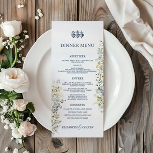 May include: A wedding dinner menu on a white plate, with floral accents and the text "Dinner Menu." The menu includes appetizers, entrees, and desserts. The menu is decorated with a floral design and the names "Elizabeth & Colten."