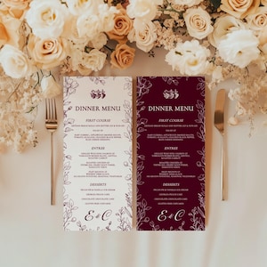 May include: Two dinner menus with floral accents and the text "Dinner Menu." One menu is white with purple text, the other is burgundy with white text. A fork and knife are placed near the menus, with a floral arrangement in the background.
