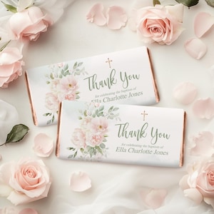 May include: Two chocolate bar wrappers with floral designs and the text "Thank You" and "for celebrating the baptism of Ella Charlotte Jones". The wrappers are decorated with pink flowers and green leaves, with a cross symbol.
