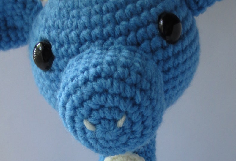 May include: Close-up of a blue crocheted stuffed animal with black button eyes. The animal has a small white nose.