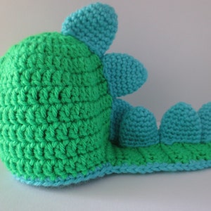 May include: A green and blue crocheted dinosaur toy with a long tail and a spiky back.