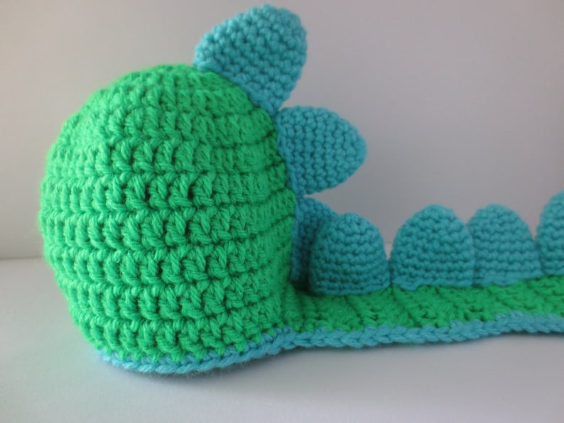May include: A green and blue crocheted dinosaur toy with a long tail and a spiky back.