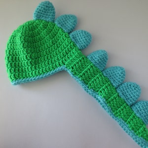 May include: Green and blue crocheted dinosaur hat with a long tail and spikes.