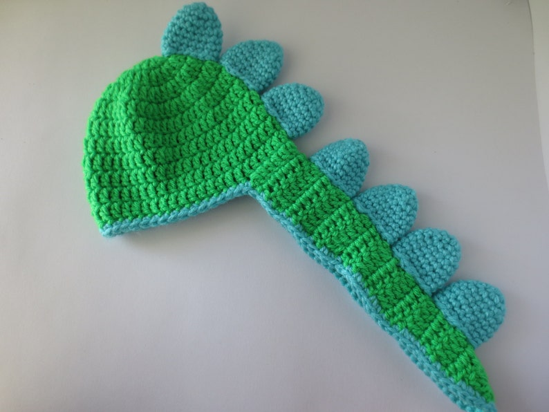 May include: Green and blue crocheted dinosaur hat with a long tail and spikes.