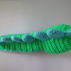 May include: A green and blue crocheted dinosaur toy with a long tail and a row of blue spikes along the back.