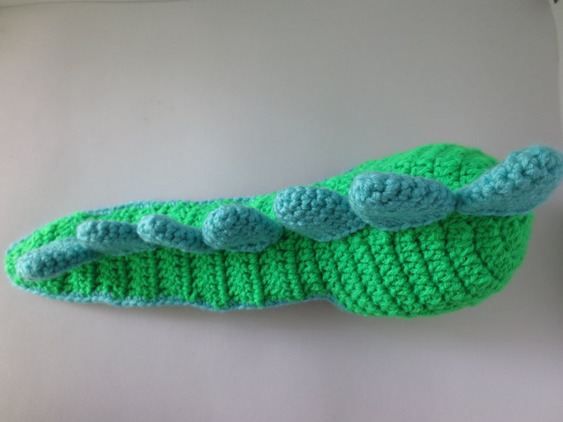 May include: A green and blue crocheted dinosaur toy with a long tail and a row of blue spikes along the back.