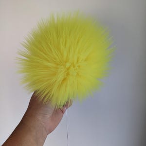 May include: A bright yellow fluffy pom pom with a white string attached.