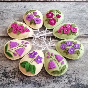 Conjunto de 4 enfeites de Páscoa em feltro nas cores amarelo pastel ou verde, com flores lilás e violeta, e ovos de Páscoa.