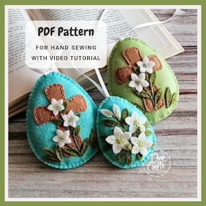 Puede incluir: Tres huevos de Pascua de fieltro, uno azul turquesa, uno verde y uno marrón, con una cruz y flores blancas bordadas en cada uno. El texto "PDF Pattern for Hand Sewing with Video Tutorial" se muestra sobre los huevos.