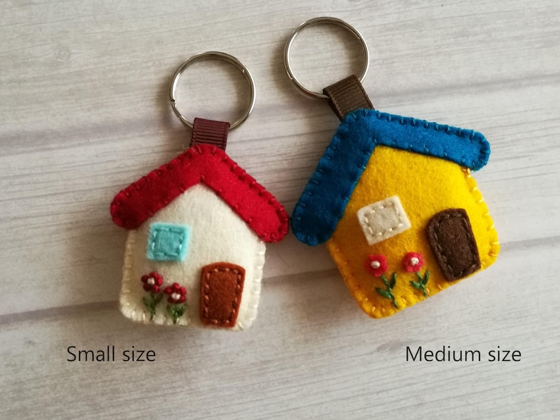 May include: Two felt house keychains. One is white with a red roof, blue window, and brown door. The other is yellow with a blue roof, white window, and brown door. Both have a brown strap and silver keyring. The text "Small size" and "Medium size" are below each keychain.