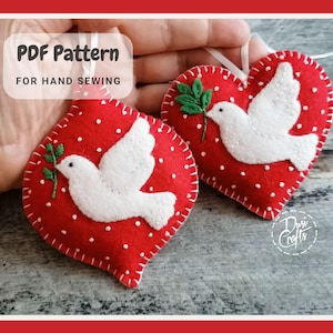 May include: Two red felt heart ornaments with white doves and green leaves. The ornaments are hand-sewn and have a white dotted pattern. The text "PDF Pattern for Hand Sewing" is at the top of the image.