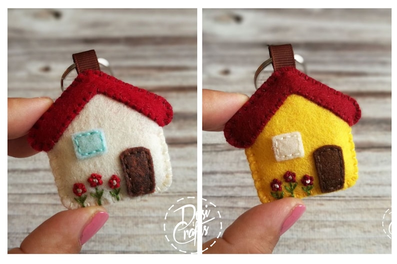 May include: A felt house keychain with a red roof, brown door, and embroidered flowers. The house has a light blue window and a brown ribbon loop for the keyring. The second house is yellow with a red roof.