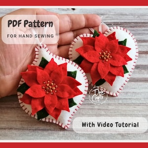 May include: Two white felt heart-shaped ornaments featuring red poinsettia flowers with green leaves and gold centers. The edges are stitched with red thread. Text reads PDF Pattern FOR HAND SEWING and With Video Tutorial.
