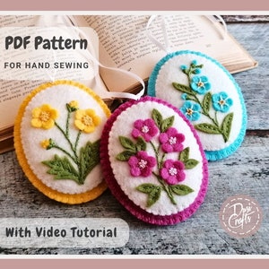 May include: Three felt ornaments with embroidered flowers. The ornaments are yellow, pink, and blue. The text "PDF Pattern for Hand Sewing" and "With Video Tutorial" is visible on the image.