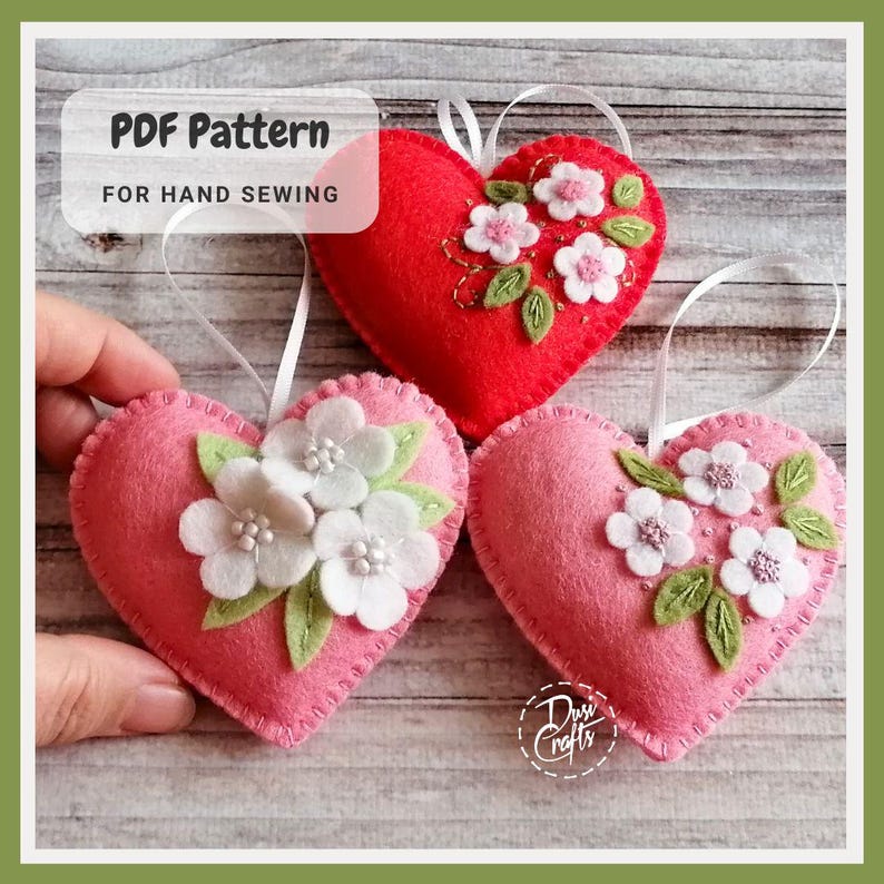 May include: Three heart-shaped ornaments in red and pink felt, adorned with white and pink floral embroidery and green leaves. Each ornament has a white ribbon for hanging. The text "PDF Pattern FOR HAND SEWING" is visible.