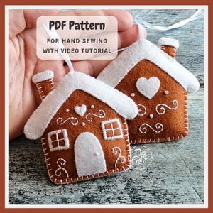K&ouml;nnte beinhalten: Zwei Filz-Lebkuchenhaus-Ornamente mit wei&szlig;en Akzenten und dekorativen N&auml;hten. Die H&auml;user haben wei&szlig;e D&auml;cher, Schornsteine und Herz- und Wirbeldetails. Der Text "PDF Pattern" und "FOR HAND SEWING WITH VIDEO TUTORIAL" ist sichtbar.