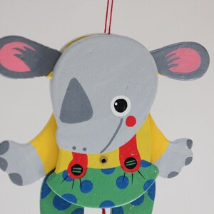 Puede incluir: Un t&iacute;tere de madera gris y amarillo de un animal de dibujos animados con orejas grandes, una nariz roja y pantalones de lunares azules y verdes. El t&iacute;tere est&aacute; colgado de una cuerda.