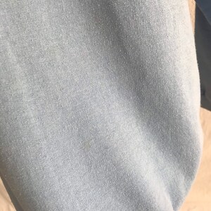 May include: Close-up of a light blue sweatshirt fabric. The fabric has a soft, textured feel.