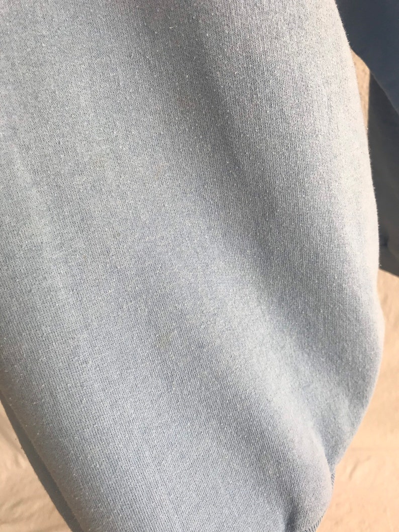 May include: Close-up of a light blue sweatshirt fabric. The fabric has a soft, textured feel.