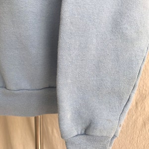 May include: A light blue sweatshirt with long sleeves and a ribbed cuff. The sweatshirt is made of a soft, comfortable fabric.