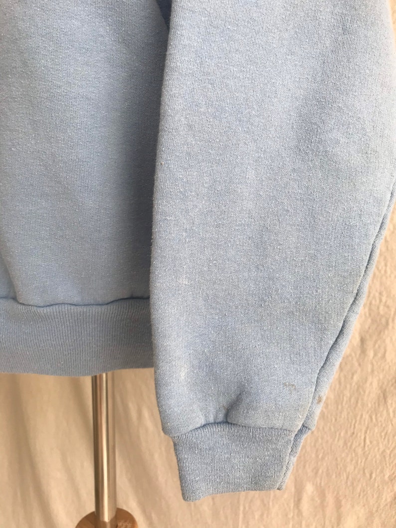 May include: A light blue sweatshirt with long sleeves and a ribbed cuff. The sweatshirt is made of a soft, comfortable fabric.
